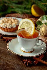 White cup of tea with lemon and meringue tartlet.
