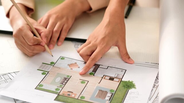 Smart architect and safety engineer discussion about building blueprint on table with architectural document, measurement tools and wooden block scatter around at modern office. Closeup. Delineation.