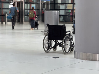 Empty wheelchair placed near column inside airport terminal hall. Mobility assistance availability, accessibility awareness, inclusive transport services, and support infrastructure concept.