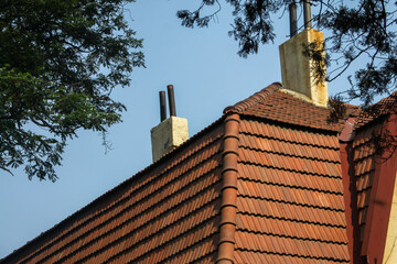 Detail of red clay roof tiles and chimney against blue sky.