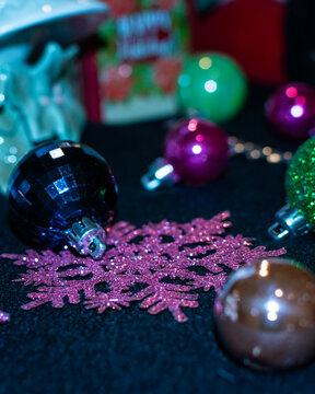 Blue Christmas tree ornament and a pink snow flake in focus while other colorful ornaments are scattered around out of focus. 