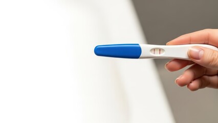 Obraz premium A close-up of a hand holding a pregnancy test with a blue cap. The test shows a positive result. The background is blurred and neutral in color.