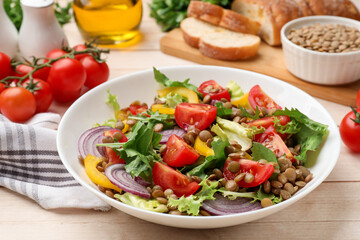 Delicious lentil salad and ingredients on light wooden table, closeup
