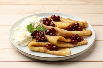 Tasty crepes with cherries, whipped cream and mint on white wooden table, closeup