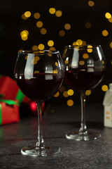 Glasses of red wine and Christmas decor on grey table against background with blurred lights
