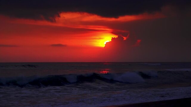 Spectacular sunset seascape with last beams of setting sun breaking through clouds, foamy ocean waves washing sand beach. Evening tropical beach, perfect vacation concept. Bali, Indonesia. Slow motion
