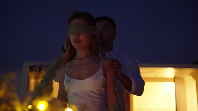 Man removes a blindfold from woman revealing a surprise, inviting to dinner for making proposal. 