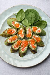 Tasty spinach crepes with salmon, cream cheese, red caviar and leaves on light grey table, top view