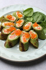 Tasty spinach crepes with salmon, cream cheese, red caviar and leaves on light grey table, closeup