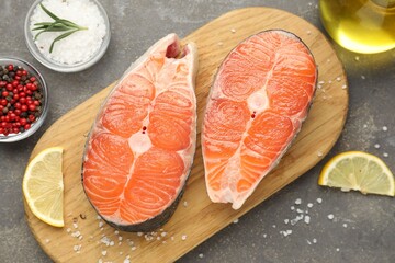 Pieces of salmon fillet with spices, lemon and oil on gray textured table, flat lay