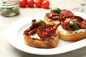 Delicious bruschettas with cream cheese, sun-dried tomatoes and green olives on gray table, closeup