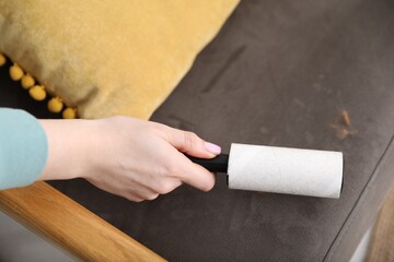 Woman cleaning armchair with lint roller at home, above view