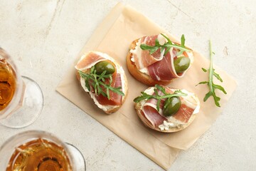 Delicious bruschettas with cream cheese, prosciutto, green olives and arugula served on gray textured table, flat lay