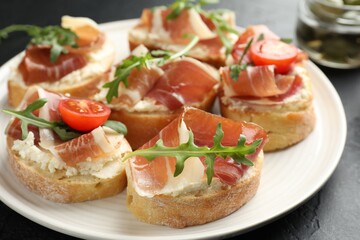 Delicious bruschettas with cream cheese, prosciutto, tomatoes and arugula on table, closeup