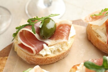 Delicious bruschettas with cream cheese, prosciutto, green olives and arugula on table, closeup