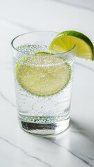 A refreshing glass of sparkling water with fresh lime slices on a white marble surface.