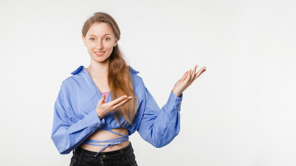 Cheerful young woman in casual outfit on white background, confidently pointing to empty space suitable for advertisement, message, slogan or graphical insertion, studio photo