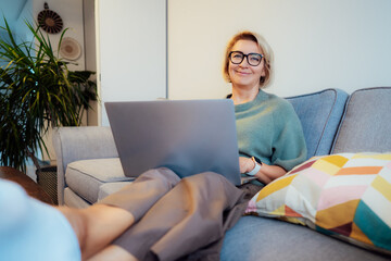 Cozy remote job. Confident Mid aged woman self employed sit on sofa at home office workplace do...