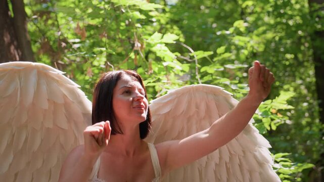 Goddess of love with angelic wings in white dress gently catches flies in sun dappled forest clearing, surrounded by lush greenery, radiating calm, curiosity, and other worldly grace