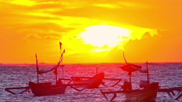 Gorgeous scene with three traditional balinese outrigger fishing vessels swaying on sea waves against sunset sky with bright setting sun and clouds on background. Evening seascape. Still camera.