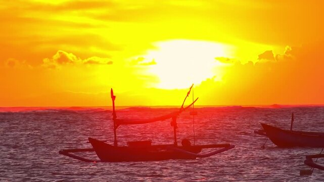 Silhouettes of traditional fishing vessels floating in ocean against red sunset sky with clouds lit by last beams of setting sun on background. Beautiful scene with evening sea. Camera stays still.