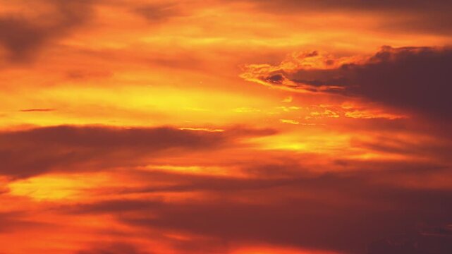 Orange sunset. Beautiful sky illuminated by last beams of setting sun. Warm evening sunlight breaking through floating clouds. Gorgeous cloudscape with fire glow of sundown. Camera stays still.