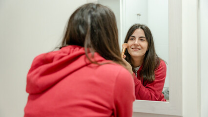 Woman applying makeup in front of mirror at home