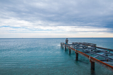 A man trying to catch fish on an iron pier.