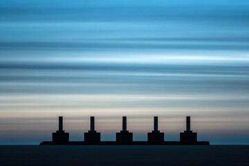 Minimalist skyline industrial silhouette factory chimney blue gradient muted tones long exposure dusk horizon calm seascape geometric symmetry quiet mood