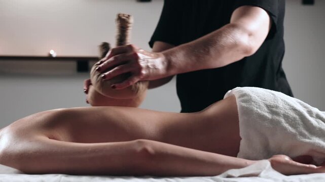 Skilled therapist uses traditional herbal pouch massage on a client&rsquo;s bare back, highlighting relaxation and wellness in a calm spa setting. Concept healing, wellness, relaxation