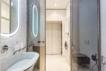 A bathroom features a tub, toilet, and laundry area. The space has a mirror with lights and clean...