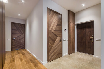 A clean hallway connects different rooms. Wooden doors are at each end. Bright lights shine from the ceiling. The floor is a mix of wood and tile, showing a modern style