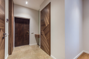 A hallway features wooden doors on both sides, soft lighting, and neutral wall colors. The entrance door is visible at the end of the space, showing a straightforward design