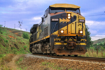 Obraz premium Powerful Freight Locomotive Approaching On Curved Railway Track Rural Countryside Showing Industrial Transportation Strength Motion Journey Through Green Hills With Dramatic Sky Rail Infrastructure