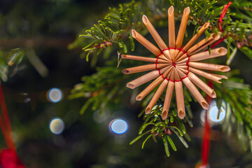 Decorated straw star ornament hanging on a Christmas tree branch during holiday season