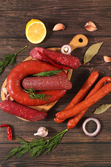 An assortment of various types of sausages, smoked meats, salami, and game sausages with lemon, spices, and herbs on a concrete table. Advertising and banner for a store, menu for a cafe or restaurant