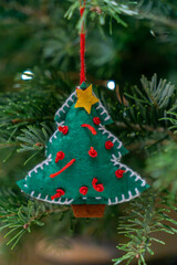 Handmade green felt Christmas tree ornament with red decorations hanging on a pine tree branch during the holiday season