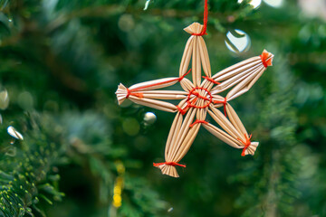 Handmade star ornament hangs on a green pine tree branch during the winter holiday season