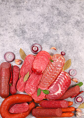 An assortment of various types of sausages, smoked meats, salami, and game sausages with lemon, spices, and herbs on a concrete table. Advertising and banner for a store, menu for a cafe or restaurant