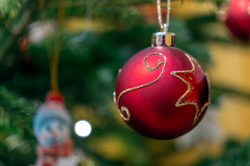 Red Christmas ornament hangs on a green tree with festive decorations and blurred lights in the background during the holiday season