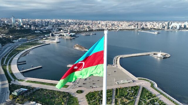 Aerial drone view of the Azerbaijani national flag waving on a high flagpole with Baku cityscape log profile background