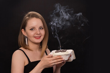 A woman in a black dress blows out a candle on a bento cake. Smoke on a black background. A girl's birthday, happiness, a gift. High quality photo