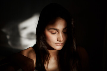 A woman with black hair wakes up in the morning in a white blanket and catches the rays of the sun. The portrait is creative, with brown eyes. High quality photo