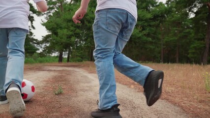 Teenagers boys kick red white soccer ball in forest. Boys play football in park. Children playing sports outdoors, healthy child. Active children, family picnic outdoors. Sports lifestyle for boys.