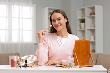Young woman with cosmetic bag and makeup products on table at home