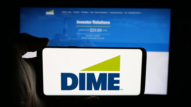 Stuttgart, Germany - 12-05-2025: Person holding cellphone with logo of US financial company Dime Community Bank on screen in front of webpage. Focus on phone display.
