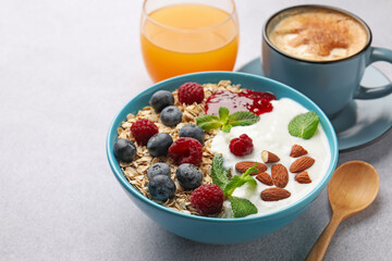 Healthy breakfast. Oatmeal with nuts, berries, yoghurt, jam, coffee and juice on grey textured table, closeup. Space for text