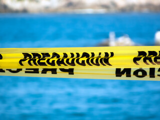 Yellow caution tape with Spanish text Precaucion cordons off a coastal area. Selective focus on the word against a blurred sea backdrop in Huatulco, Oaxaca, Mexico.