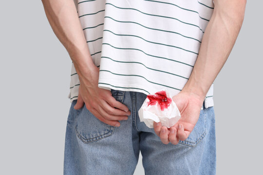 Young man holding paper with blood on light background, back view. Hemorrhoids concept