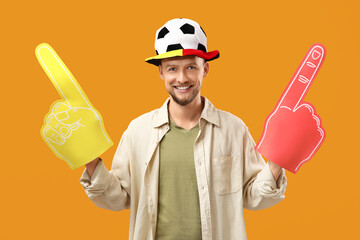 Male German soccer fan with foam hands on orange background